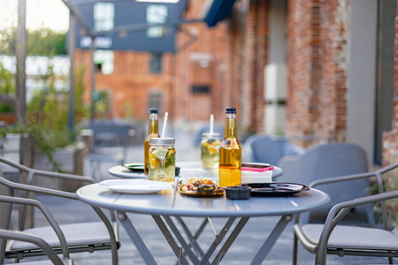 An outdoor restaurant table set for service, with drinks and food items on a sunny day, no people.の写真素材