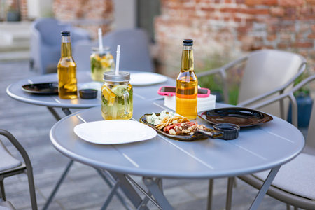 An outdoor restaurant table with drinks, food, and plates, ready for guests. No people are present.の写真素材
