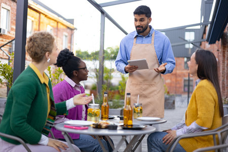 A waiter taking orders from a group of friends at an outdoor cafe, using a tablet device.の写真素材