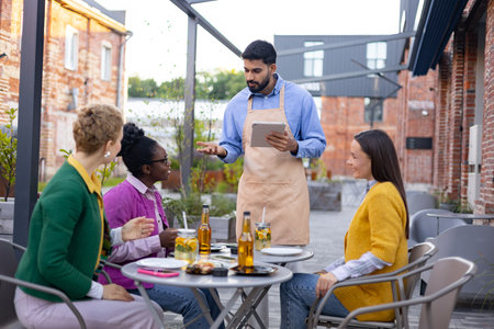 A waiter takes an order on a tablet from customers at an outdoor restaurant.の写真素材