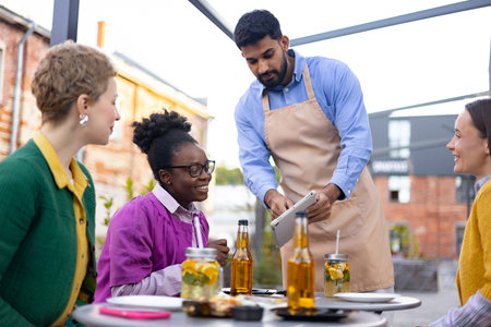 A server takes an order from customers at an outdoor cafe, showcasing a multicultural dining experience.の写真素材