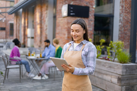 A smiling waitress takes an order on a tablet at an outdoor restaurant.の写真素材
