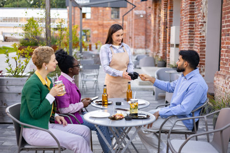 A female waiter hands a portable terminal to a customer at a restaurant. People are sitting at a table.の写真素材