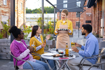A group of friends enjoying sushi and drinks at an outdoor restaurant, served by a friendly waitress.の写真素材