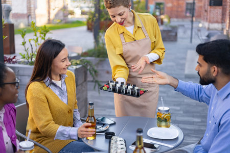 A smiling waitress serving sushi to a group of friends at an outdoor restaurant.の写真素材