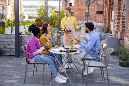 A group of friends are served sushi by a waitress in a restaurant, enjoying outdoor dining.の写真素材