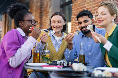Diverse group of friends enjoying sushi and drinks outdoors, creating a relaxed and joyful dining...