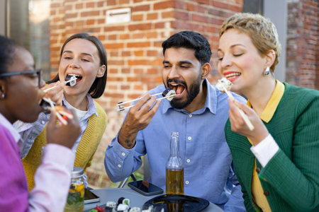 A diverse group of friends enjoys a sushi meal together, savoring the flavors and company outdoors.