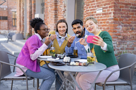 A diverse group of friends enjoys sushi and takes a selfie at an outdoor cafe.の写真素材