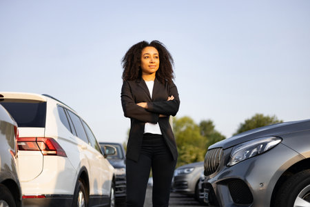 A confident woman in a business suit standing near cars, possibly a car saleswoman or manager, with a look of assurance.の写真素材