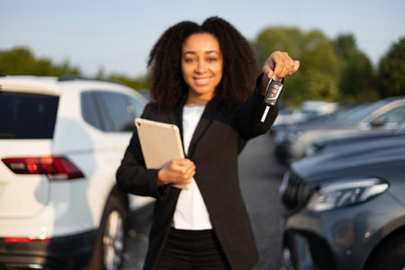 A smiling woman holds a car key, symbolizing a successful car sale or dealership transaction, showcasing the joy of ownership and purchase in an outdoor setting.の写真素材