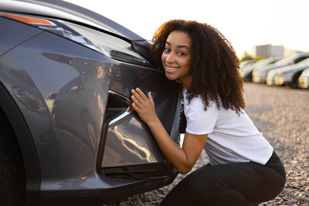 A smiling woman is happily embracing a new car shes about to purchase. A car dealership with a gray car.の写真素材