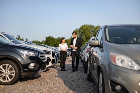 A male car dealer assisting a female customer in a car lot, discussing vehicle options and features.の写真素材