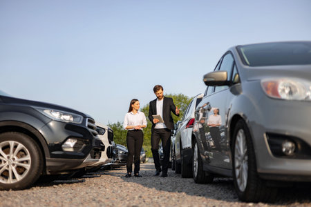 A male car dealer presents a vehicle to a woman at a car dealership, discussing options and...