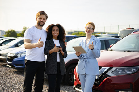 Three people at a car dealership giving a thumbs up in front of a red car, showcasing customer satisfaction.の写真素材