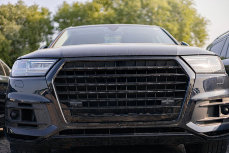 A close-up of a black SUVs front, showcasing its grill and headlights, parked outdoors with other vehicles in view.の写真素材
