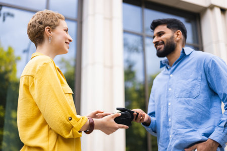 A smiling man and woman are shown making a payment using a mobile payment device outdoors, near a building.の写真素材