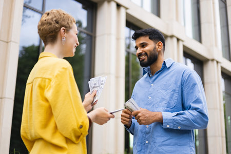 A woman hands money to a man outdoors, likely a financial transaction, against a building.の写真素材