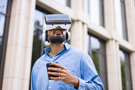 A man wearing a VR headset drinks coffee outdoors, experiencing virtual reality in an urban setting.