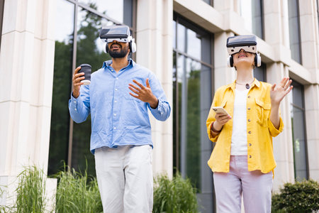 A diverse couple experiences virtual reality outdoors. They wear VR headsets and interact with their...