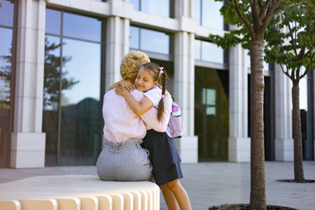 A mother and daughter share a warm embrace outside a school building, a symbol of love and support.の写真素材