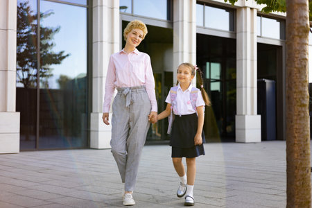 A mother and her elementary student daughter walk together in a schoolyard, holding hands and smiling.の写真素材