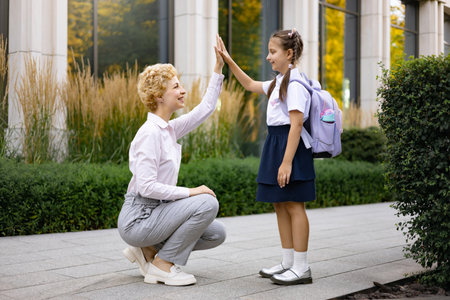 A mother and her daughter share a high-five in a schoolyard, celebrating a moment of connection.の写真素材