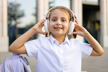 A Caucasian schoolgirl in a white shirt and headphones smiles at the camera in the schoolyard.