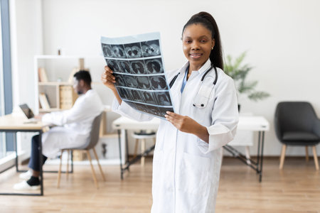 Young female doctor holding X-ray film in hospital office, male colleague working background
