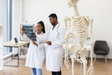 Focused male and female doctors analyzing X-ray images, medical skeleton in foreground, study...