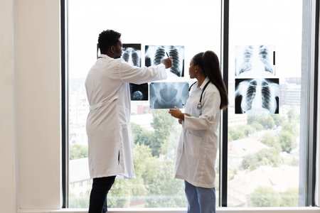 Medical professionals, male and female, reviewing x-ray diagnoses near a bright clinic window....
