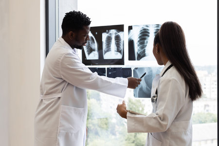 Male and female doctors of diverse backgrounds examining chest X-ray images by window. Collaborative...