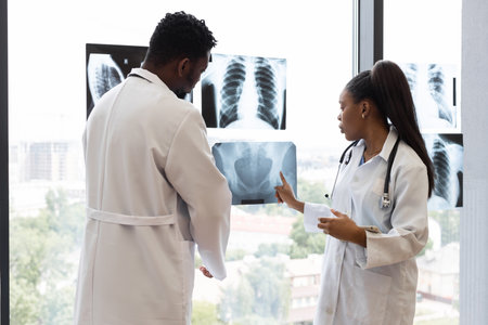 Male and female doctors of diverse backgrounds examining chest X-ray images by window. Collaborative medical consultation in modern clinic setting, emphasizing teamwork, analysisの写真素材