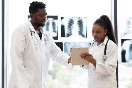 Male and female doctors communicating in medical setting with x-rays displayed near window indoors