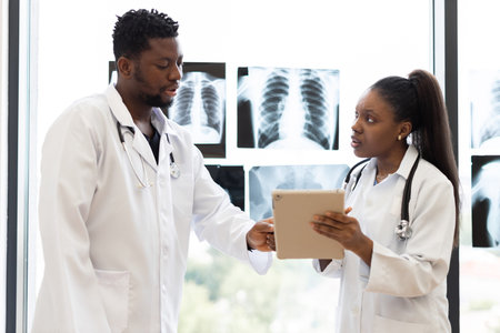 Male and female doctors discussing patient diagnosis in a clinical environment with x-rays visible....