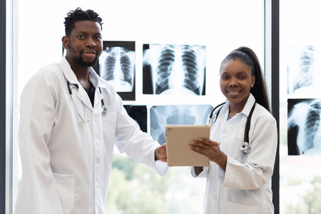 Two medical professionals, male and female, standing in clinic near window discussing x-rays, radiating professionalism and teamwork, symbolizing health care, dedication, expertise.の写真素材