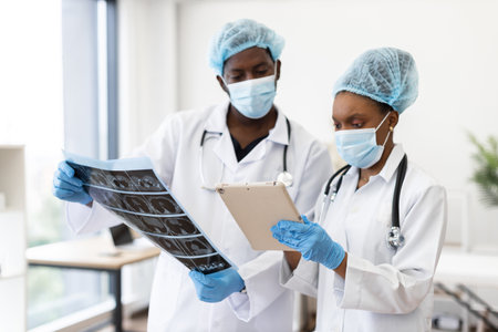 Two adult medical professionals discussing diagnostics, one viewing scans and one holding clipboard, collaborative environmentの写真素材