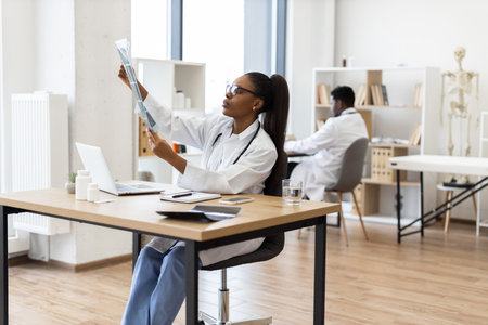 Young African woman doctor analyzing x-ray image at desk in contemporary clinicの写真素材