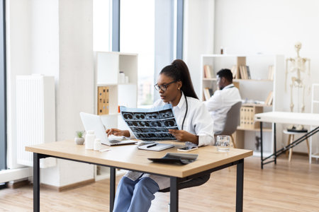 Young adult doctors, male and female, reviewing radiography scans on laptops at workplace depicting diagnostic and healthcare scenario indoors.の写真素材