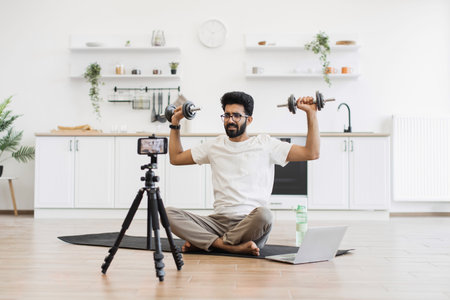 Man exercising with dumbbells during video recording in kitchen, showcasing fitness routine and...