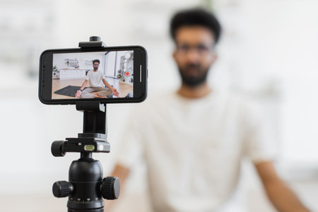 Young adult male sitting in meditative pose recording health video blog on smartphone.の写真素材