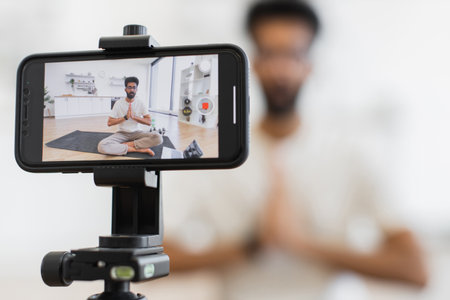 Young adult man explaining meditation benefits, seated on yoga mat indoors, recording video.の写真素材