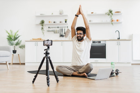 Young adult man practicing meditation, recording wellness video content in serene kitchen environment. Promotes healthy lifestyle, mindfulness exercise, and content creation for online teachingの写真素材