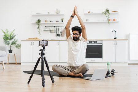 Young adult man practicing meditation, recording wellness video content in serene kitchen environment. Promotes healthy lifestyle, mindfulness exercise, and content creation for online teachingの写真素材