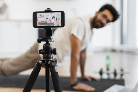 Young man performs plank pose indoors, recording video tutorial for health enthusiasts using modern...
