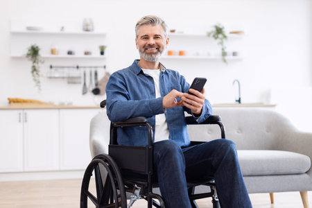 Mature Caucasian man seated in wheelchair holding smartphone in contemporary home interior...