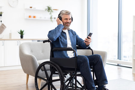 Mature Caucasian man in wheelchair enjoying music wearing headphones and using phone in bright...