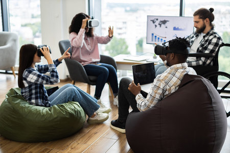 Group of diverse adults using virtual reality headsets and laptops in modern office setting....