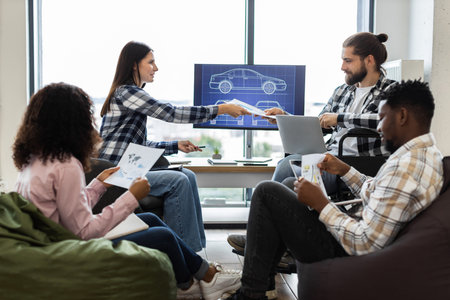 Four young adults collaborating on car project in modern office. Ethnically diverse group focused on...
