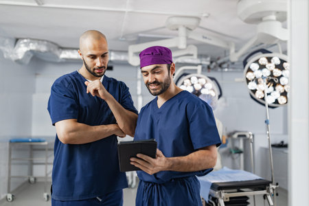Two surgeons in scrubs review a tablet in an operating room, discussing a procedure with focused...